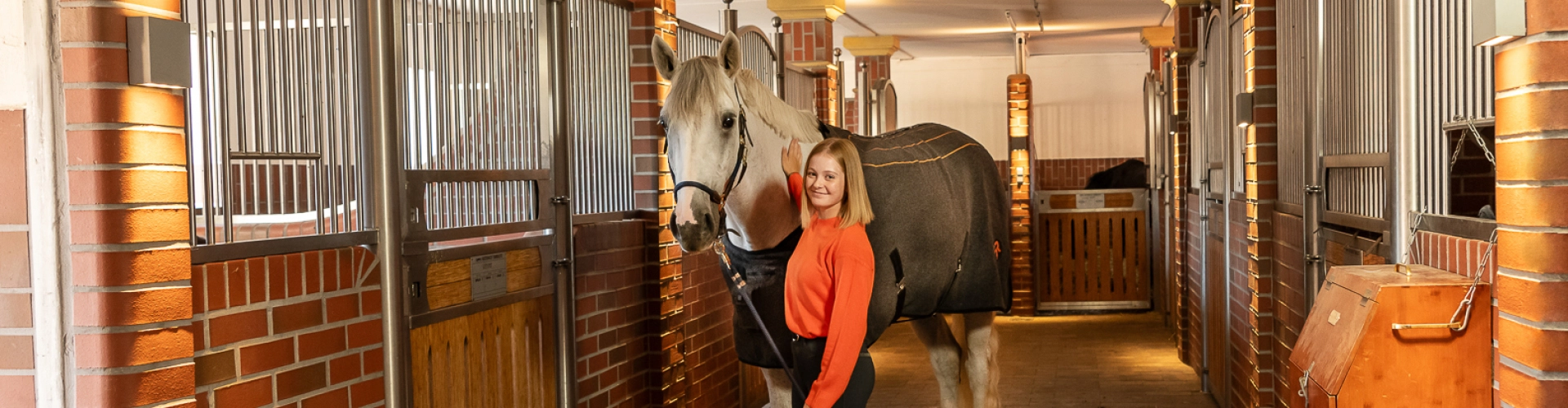 A horse stands in the stable next to its rider, wearing the St. Moritz heated blanket.