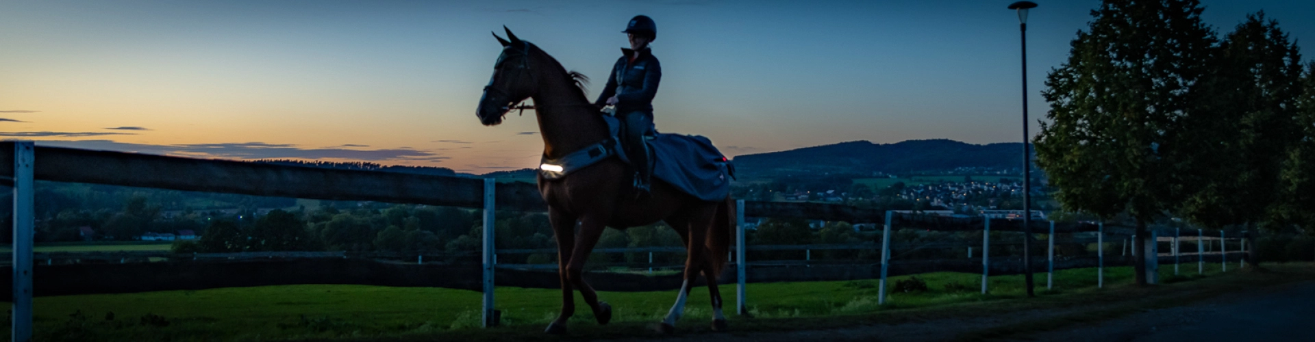 LED Ausreitdecke New York in grau Ein Pferd und Reiter mit der New York LED Ausreitdecke in der Daemmerung