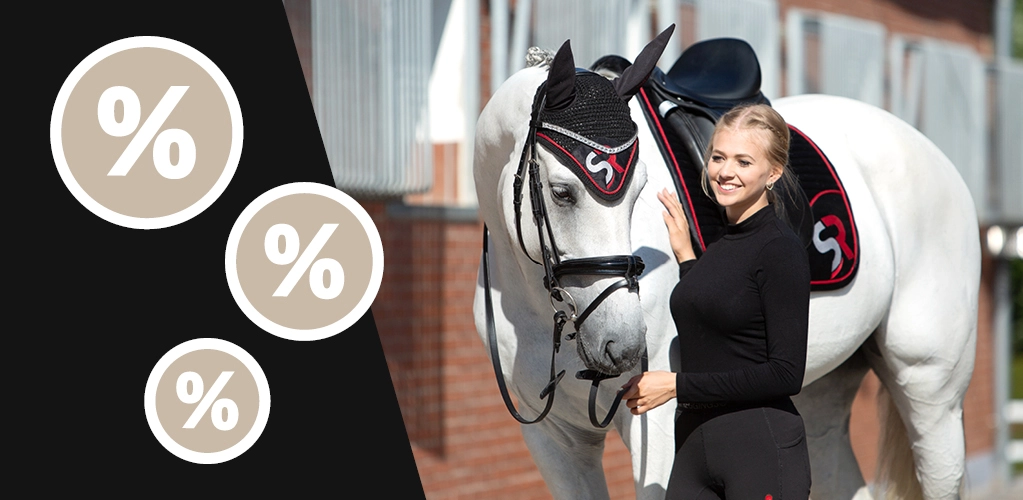 Eine Reiterin steht neben einem Pferd mit schwarz roter Schabracke und passender Fliegenhaube mit SR Logo im Hintergrund ist ein Stall