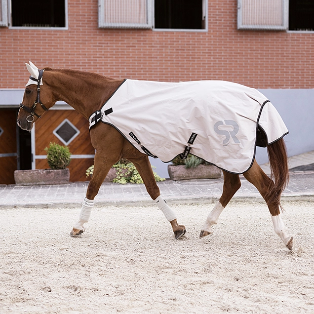 Ein Pferd läuft auf einem Sandplatz und trägt eine beige Führanlagendecke Cornwell von Sunride