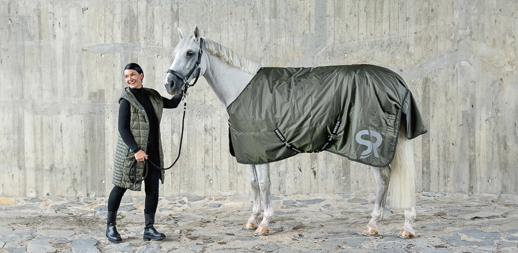 Winterdecke Ein Reiter steht einem Pferd gegenüber Das Pferd trägt eine dunkelgrüne Decke von Sunride Liverpool Modell