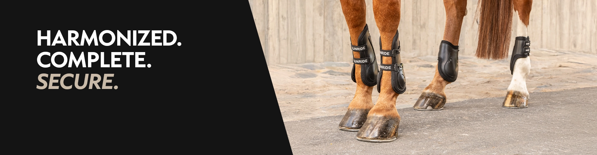 Four horse legs with brown boots and fetlock protectors on asphalt in front of a wall with the text Harmonized Complete Secure on the left