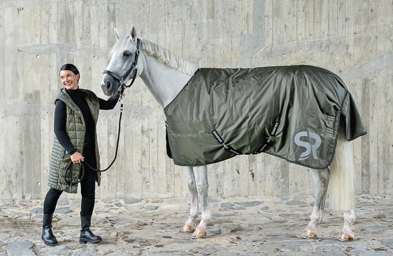 Winterdecke Ein Reiter steht einem Pferd gegenüber Das Pferd trägt eine dunkelgrüne Decke von Sunride Liverpool Modell