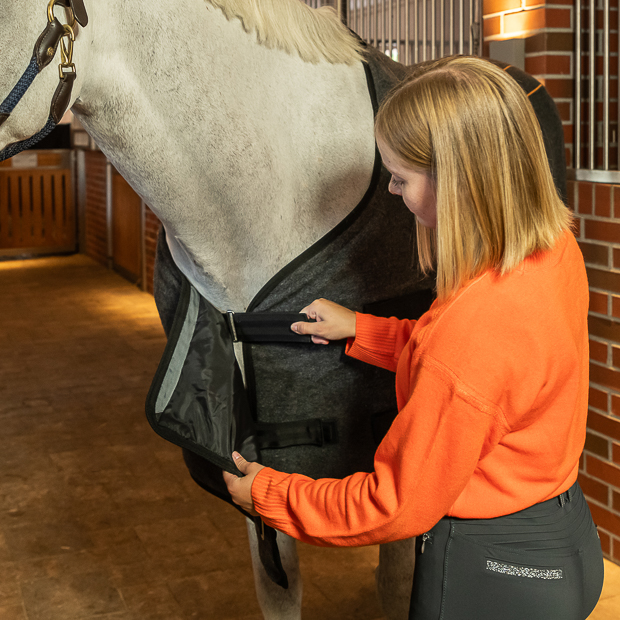front closure of grey heating rug st. moritz from wool on horse with rider grey wool heating rug st. moritz with three levels of heating and program on a horse in the stable with rider on front closure